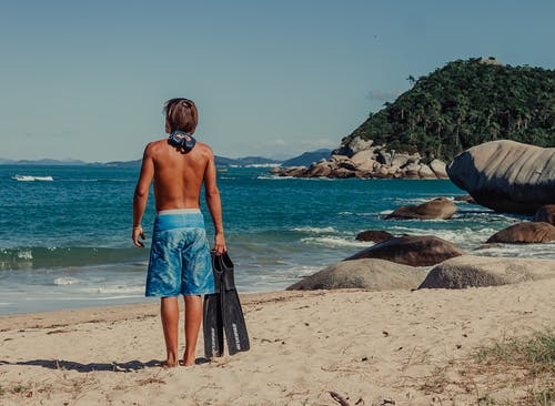 男人穿着蓝色短裤，站在海滩上 · 免费素材图片