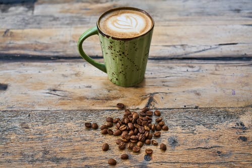 杯卡布奇诺咖啡桌上的咖啡豆 · 免费素材图片
