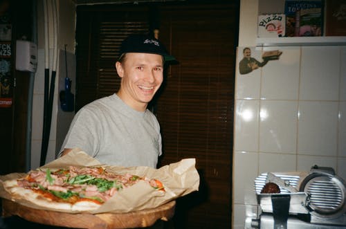 站立和微笑着拿着披萨的男人 · 免费素材图片