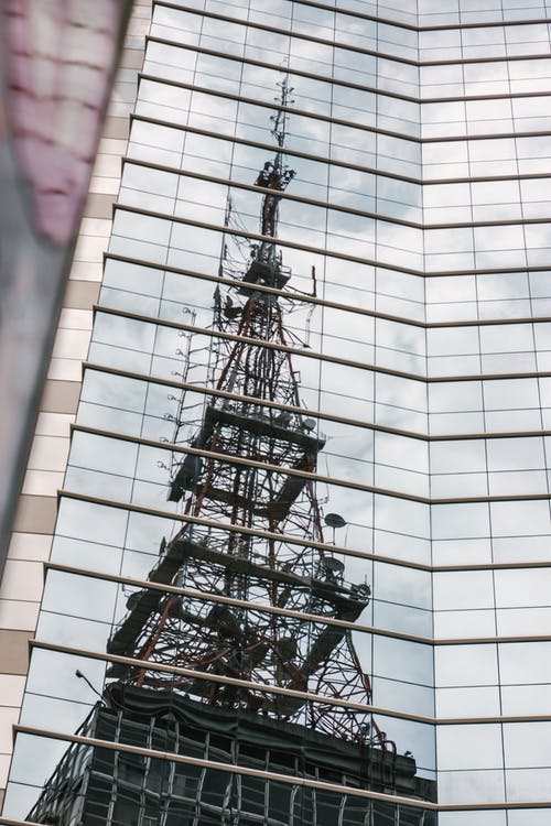 灰色钢塔在建筑玻璃墙上的反射 · 免费素材图片