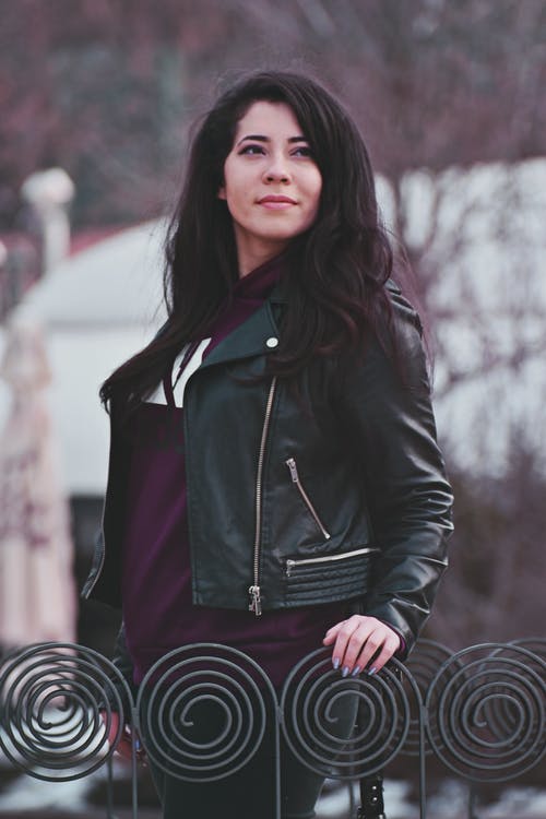 拿着灰色金属栏杆的黑色皮夹克的女人的照片 · 免费素材图片