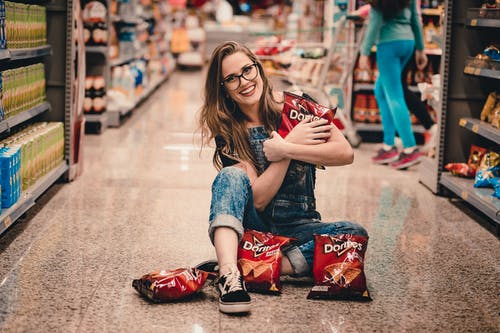 坐在购物过道中间的微笑妇女的照片拿着dorito芯片 · 免费素材图片