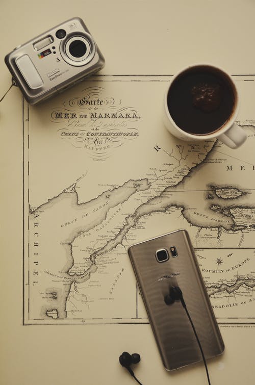 银相机，金质智能手机和黑色耳塞附近的杯子中的黑咖啡 · 免费素材图片