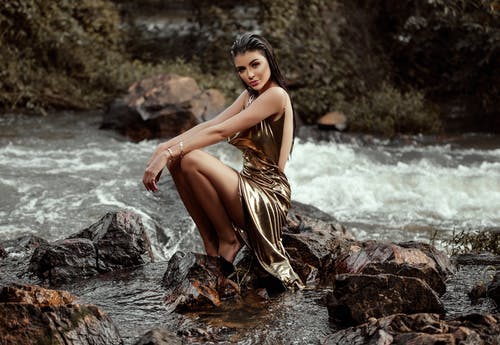 金礼服坐在河边的岩石上的女人 · 免费素材图片