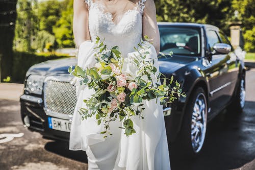 白色的婚纱，在黑色的车前携带花束的女人 · 免费素材图片
