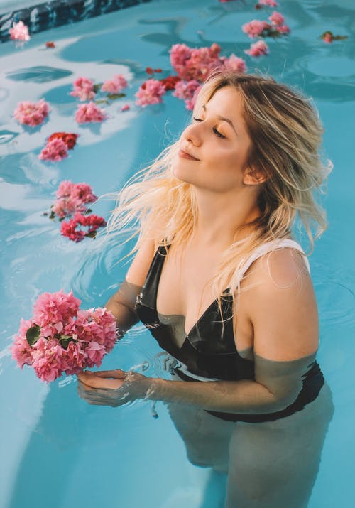女人在游泳池里捧着粉红色的花朵 · 免费素材图片