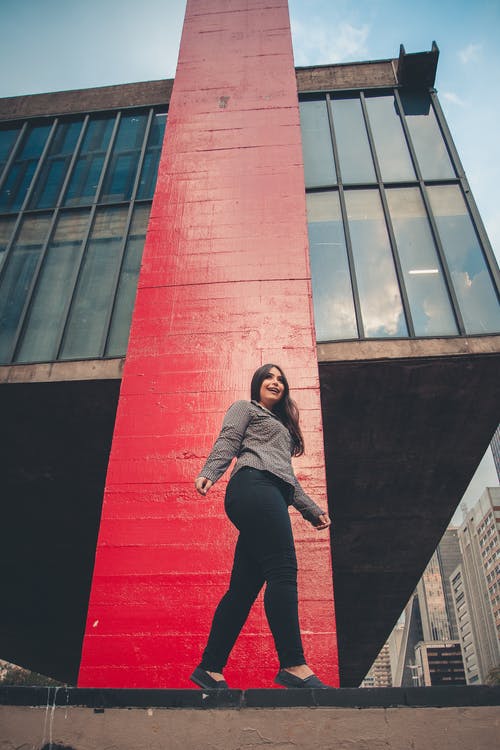 低角度的微笑的女人站在建筑物旁边她的脚趾的照片 · 免费素材图片