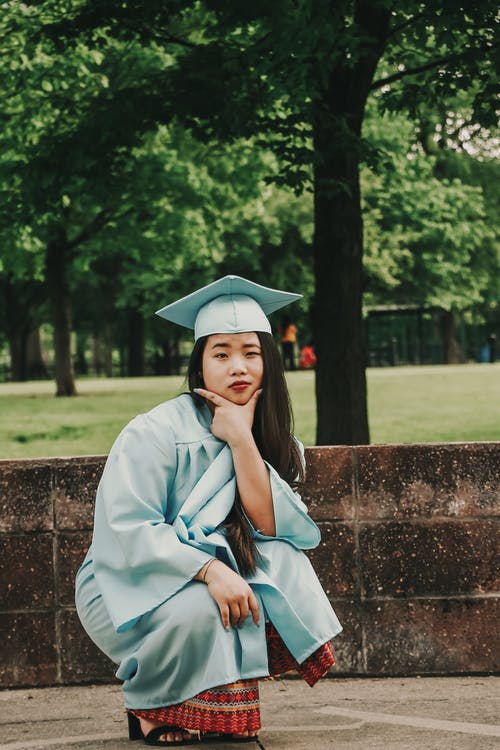 蹲下的女人，穿着蓝色的学术礼服和帽子 · 免费素材图片
