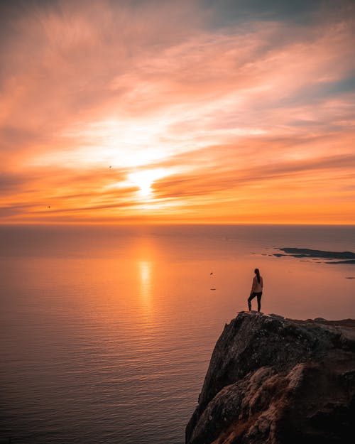 在日落期间站在悬崖上的人 · 免费素材图片
