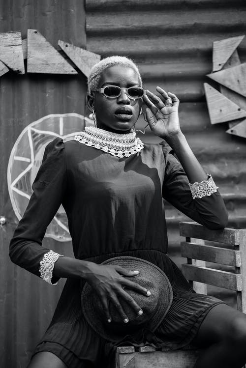 戴着太阳镜坐在椅子上的男孩穿裙子的灰度摄影 · 免费素材图片