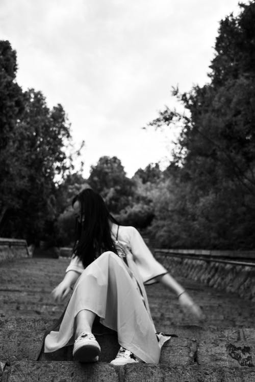 女人坐在混凝土楼梯上的低角度灰度照片 · 免费素材图片