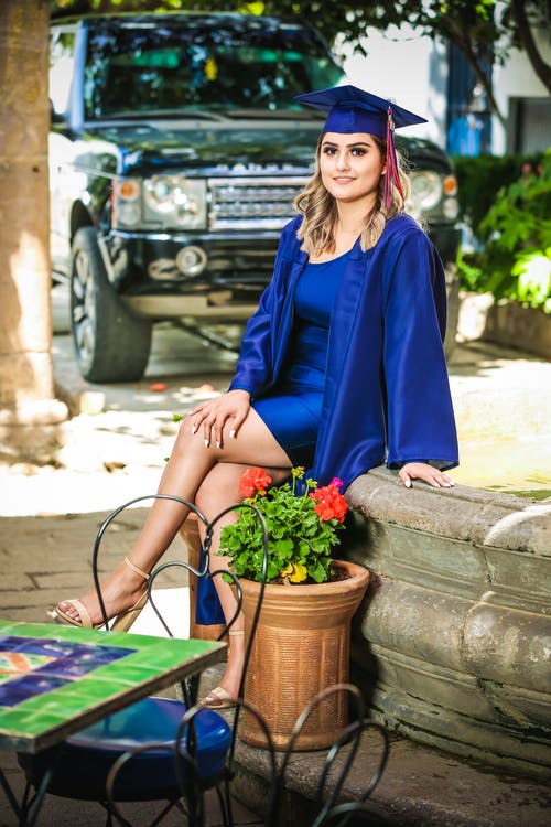 女人穿着蓝色毕业礼服坐在盆栽的植物旁边 · 免费素材图片