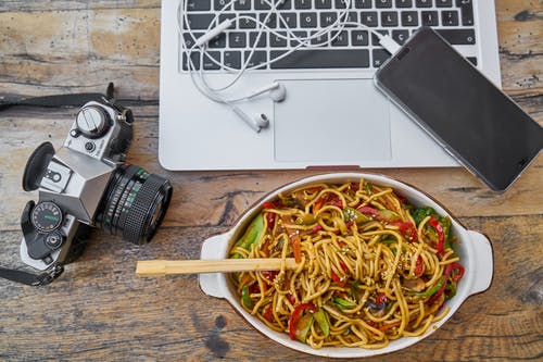 单反相机和便携式计算机旁边碗上的面食 · 免费素材图片