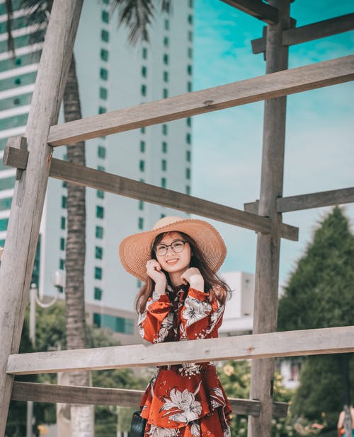 倾斜在木结构的太阳帽子和花服的微笑的妇女照片 · 免费素材图片