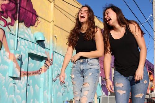 两个笑着的女人走过涂鸦墙的照片 · 免费素材图片