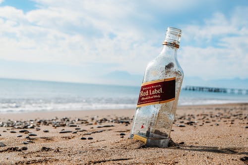 棕色沙滩上的红色标签玻璃瓶 · 免费素材图片