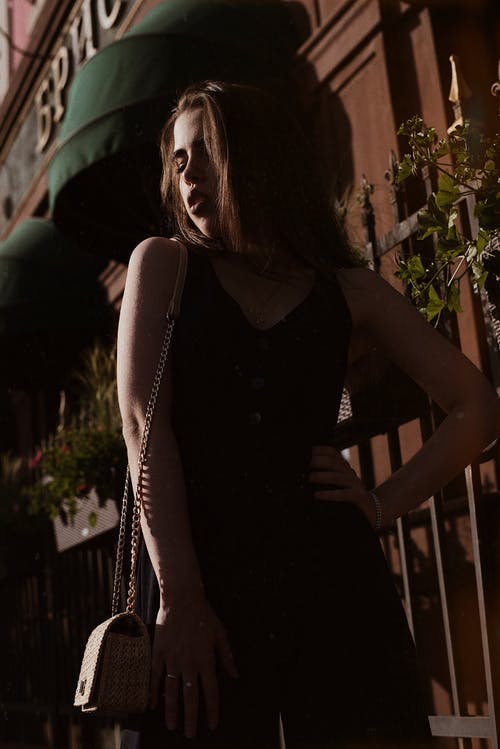 黑色无袖连身裤和斜挎包在大楼附近摆姿势的女人的照片 · 免费素材图片