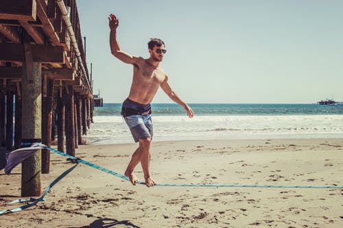 男子站在海滩附近的绳子上 · 免费素材图片