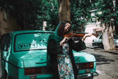 女人靠绿色车辆时拉小提琴 · 免费素材图片