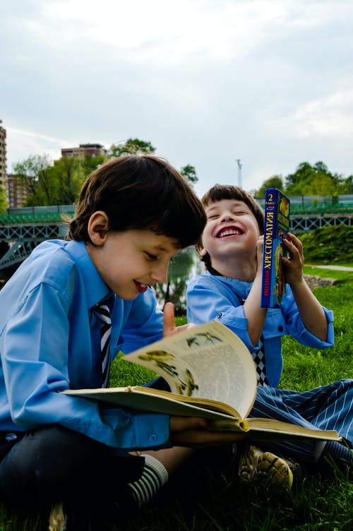 两个男孩坐在草地上笑着看书 · 免费素材图片