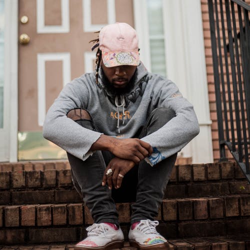 灰色连帽衫，灰色做旧牛仔布牛仔裤和粉红色帽子坐在房子前面台阶上的男人 · 免费素材图片