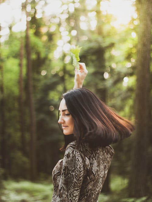 拿着绿叶的微笑的女人的侧视图照片 · 免费素材图片