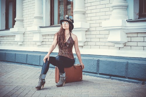 女人坐在大楼前的棕色手提箱上的照片 · 免费素材图片