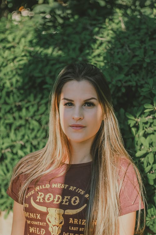站在绿色叶子的植物前面的棕色t恤的肖像照片女人 · 免费素材图片