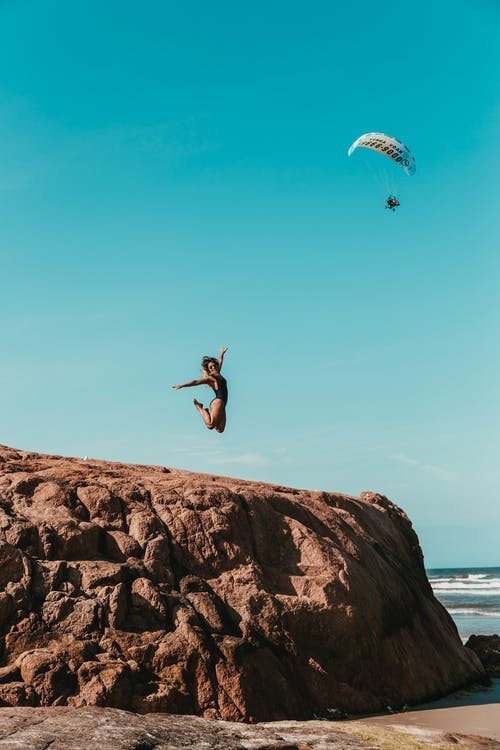 女人跳上棕色岩层 · 免费素材图片