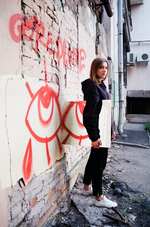 女人穿着连帽衫和黑色的裤子站在墙附近的照片 · 免费素材图片