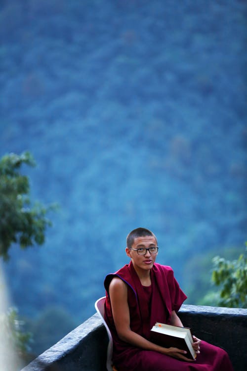 拿着棕色的书，坐在粉红色的椅子上的人 · 免费素材图片