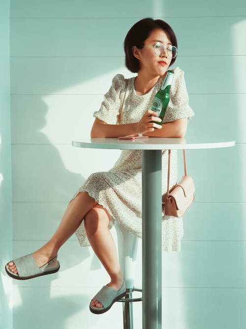 女人坐在桌旁拿着瓶 · 免费素材图片