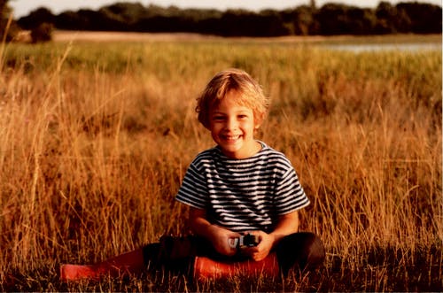 男孩坐在棕色的草地上 · 免费素材图片