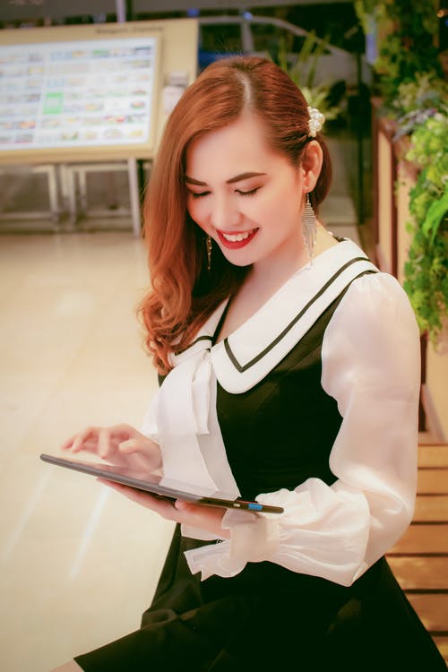 使用平板电脑的黑白衣服站立的微笑女人的照片 · 免费素材图片