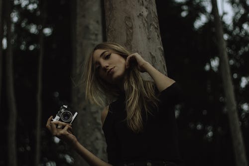 拿着照相机站立在树下的妇女的低角度照片 · 免费素材图片