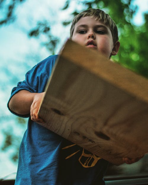 男孩抱着木板的低角度照片 · 免费素材图片