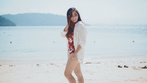 在海滩上摆姿势的花卉泳装和白色礼服衬衫的女人的照片 · 免费素材图片