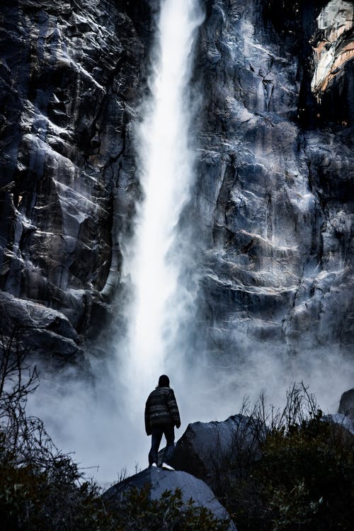 男子站在瀑布附近 · 免费素材图片
