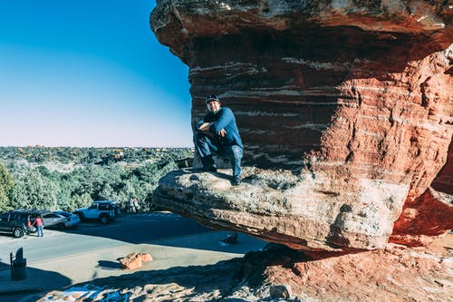 男子坐在棕色岩层 · 免费素材图片