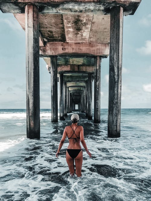 女人的比基尼站在木制的海滨码头下面的背影照片 · 免费素材图片