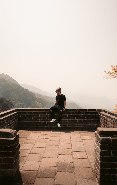 男子坐在棕色砖阳台上 · 免费素材图片
