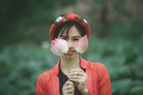 微笑的女人举起粉红色的莲花在她的脸前的选择性焦点照片 · 免费素材图片