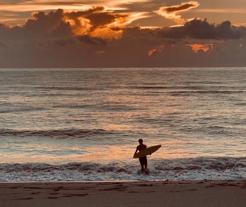 黄金时段男子在海边携带冲浪板的照片 · 免费素材图片