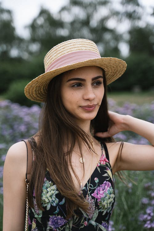 女人在太阳帽子和花裙子站在花田中的选择性焦点肖像照片 · 免费素材图片