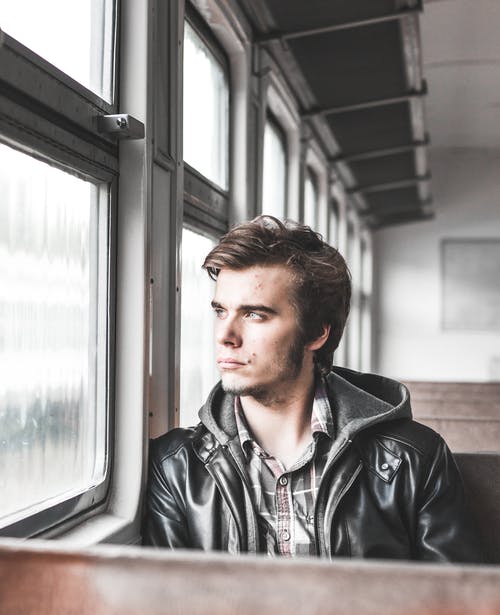 坐在火车上，看着窗外的男人的照片 · 免费素材图片