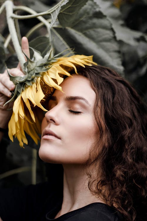 女人的侧视图肖像照片，她的眼睛闭上摆在脸上的黄色向日葵 · 免费素材图片