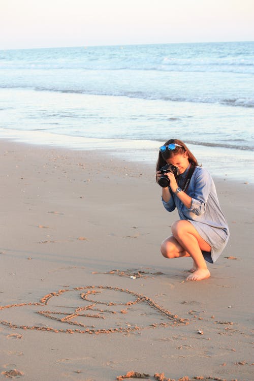 女人在沙滩上拍心形照片的照片 · 免费素材图片