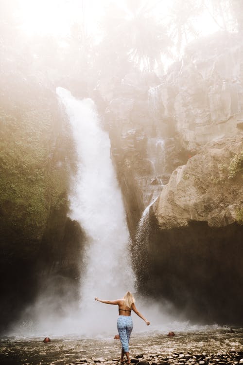 裤子在瀑布附近的石头上行走的女人 · 免费素材图片