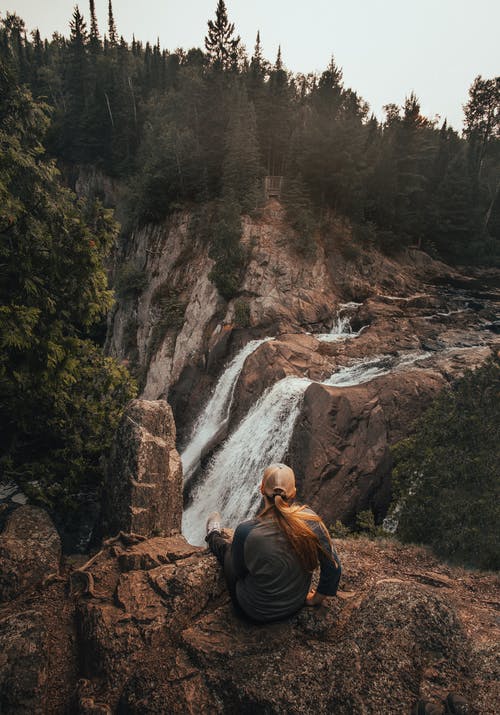 凝视瀑布时坐在岩石上的女人 · 免费素材图片