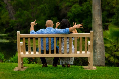 夫妇坐在棕色的木凳上，伸出他们的手，用他们的手指拼写单词爱的后视图照片 · 免费素材图片